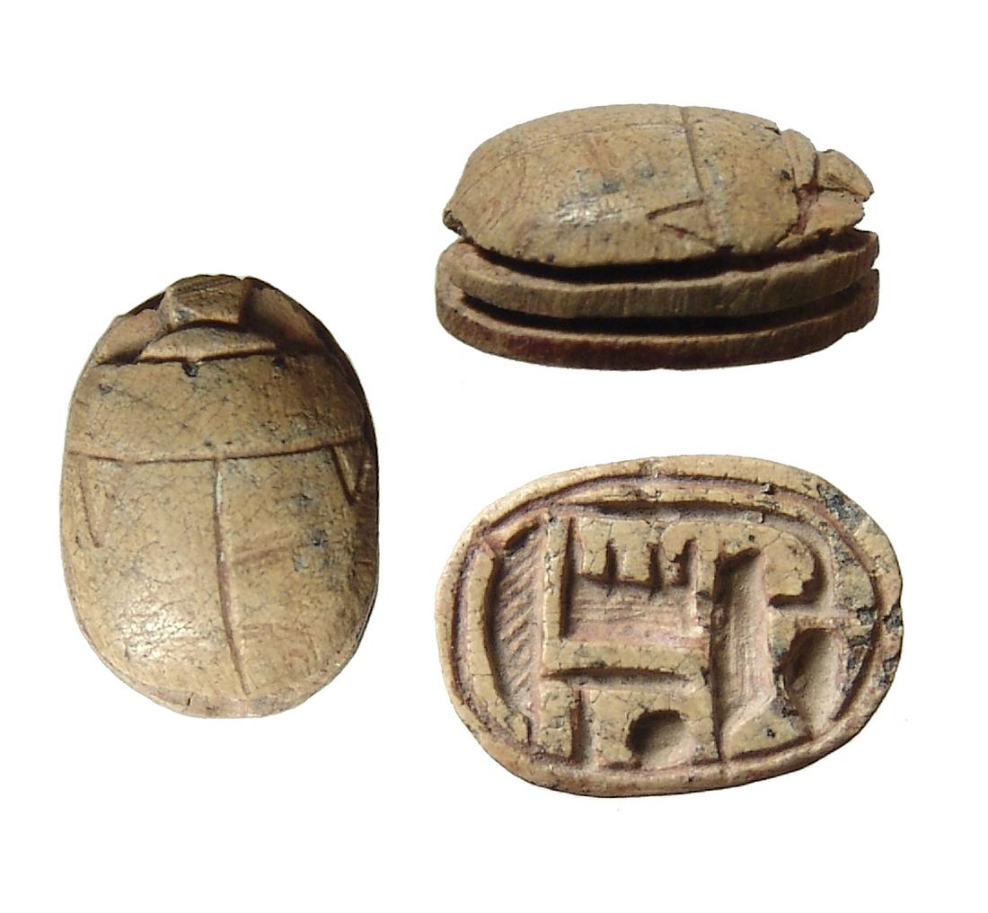 An Egyptian brown steatite scarab, Late Period: An Egyptian brown steatite scarab, Late Period, 25th - 26th Dynasty, c. 764 - 525 BC, the body domed with grooved legs, on base 'Amun-Ra' with neb sign and an ankh at end of lotus blossom. 14 x 10 mm.