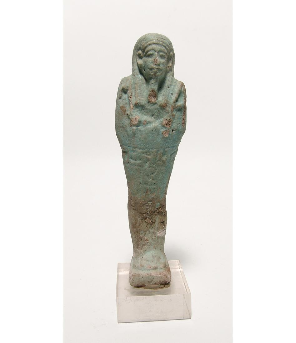 A large Egyptian pale blue-green faience ushabti: A large Egyptian pale blue-green faience ushabti, c. 664 - 332 BC, on integral base, mummiform wearing striated tripartite wig and false beard, arms folded at chest, hands holding a pick and hoe, bask