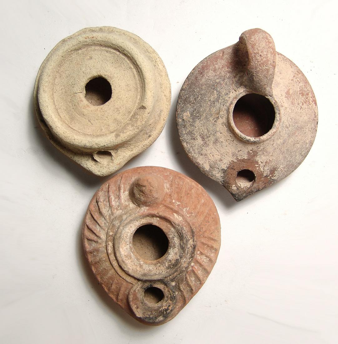 A group of 3 ceramic lamps from the Holy Land: A group of 3 ceramic lamps from the Holy Land. Lot includes a Byzantine type, c. 6th - 7th Century AD, with raised lines around the shoulders, conical handle and beautiful decorated cruciform device a