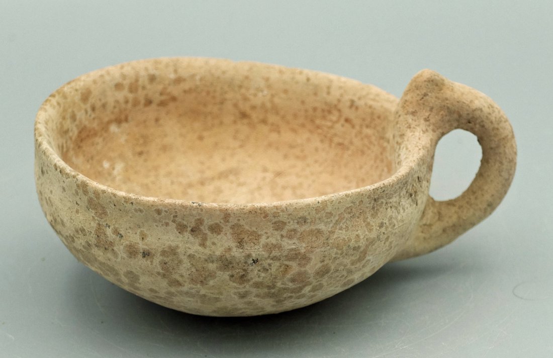 An Early Bronze Age ceramic cup, Holy Land: An Early Bronze Age ceramic cup, Holy Land, c. 3150 - 2200 BC, the hemispherical bowl with flared rim and handle with decorative element. Dia: 4 ¼ in (10.7 cm). Nice example with strong mineral encru