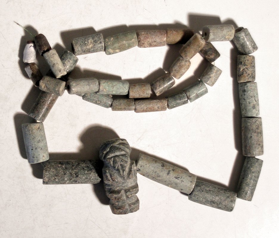 A beautiful Tairona greenstone necklace: A beautiful Tairona greenstone necklace, Colombia, c. AD 1000 - 1500, featuring a central figural pendant. This ancestral figure or elder is well detailed and nicely polished, and shown with a distend