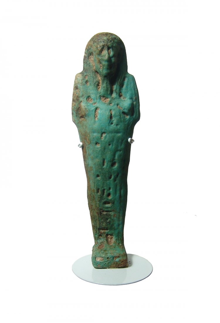 An Egyptian blue-green faience ushabti, Late Period: An Egyptian blue-green faience ushabti, Late Period, c. 664 - 332 BC, depicted mummiform on integral base, wearing tripartite wig with false beard, arms folded at chest and holding a pick and hoe. At 