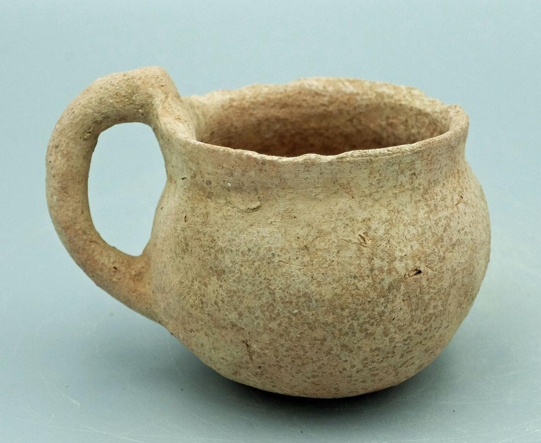 An Early Bronze Age ceramic cup, Holy Land: An Early Bronze Age ceramic cup, Holy Land, c. 3150 - 2200 BC, with flared rim and intact loop handle. Dia: 3 1/4 in (8.3 cm). Nice example with strong mineral encrustation. Ex Ancient Artifacts & Tre