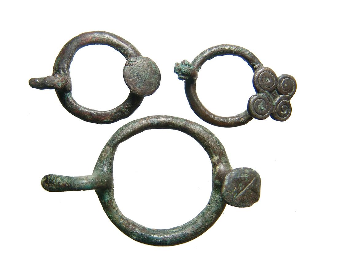 A lot of 3 decorative bronze fasteners, Central Asia: A lot of 3 decorative bronze fasteners, Central Asia, c. 1200 - 600 BC, each with circular body with raised stud of chape, one adorned with 4 discs with spiral pattern. The prongs are angles outward, 