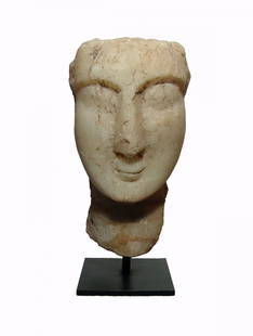 A Sabaean marble head of a man: A Sabaean marble head of a man, c. 1st Century AD, with angular features, large eyes and pursed lips. The top and back of the head are flattened, as is typical of the type. H: 9 1/4 in (23.5 cm).