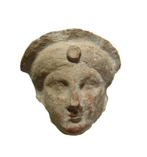 A Greek terracotta face of a goddess: A Greek terracotta face of a goddess, 5th Century BC, wearing a tall diadem with central raised disk, her features are stoic. Likely from a protome. 3 1/2 x 3 3/8 in (8.9 x 8.6 cm). Light deposits.