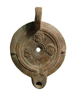 Roman lamp with theater masks decorating discus: A Roman lamp with theater masks decorating discus, 2nd Century AD, bordered by ridges, the spout rounded with ring handle. L: 2 1/8 in (10 cm). Remnants of orange-brown slip, losses to bottom. Cf.