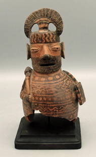 A beautiful Gallinazo-Viru figural bust: A beautiful Gallinazo-Viru figural bust, c. AD 1 -100, depicting an ornately attired warrior holding a club in one hand and his shield in the other. He is adorned with a fancy tumi-form headdress,