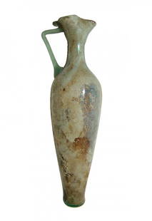 A Roman pale blue-green glass pitcher: A Roman pale blue-green glass pitcher, Eastern Mediterranean, 4th Century AD, the body tapering to a narrow flattened foot and lightly pinched, rounded shoulders. The tubular neck with trefoil