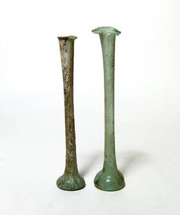 A pair of Roman pale green glass unguentariums: A pair of Roman pale green glass unguentariums, c. 2nd - 3rd Century AD, each with small bell-shaped bodies and indented bottoms, their necks very tall and narrow with flared mouths. H: 5 in (12.7