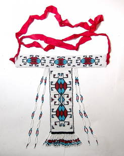 A lovely Native American beaded ornamental sash: A lovely Native American beaded ornamental sash, a type worn by young girls. The beautiful geometric designs are bold against the white background, a red ribbon ties it in place. Main beaded element