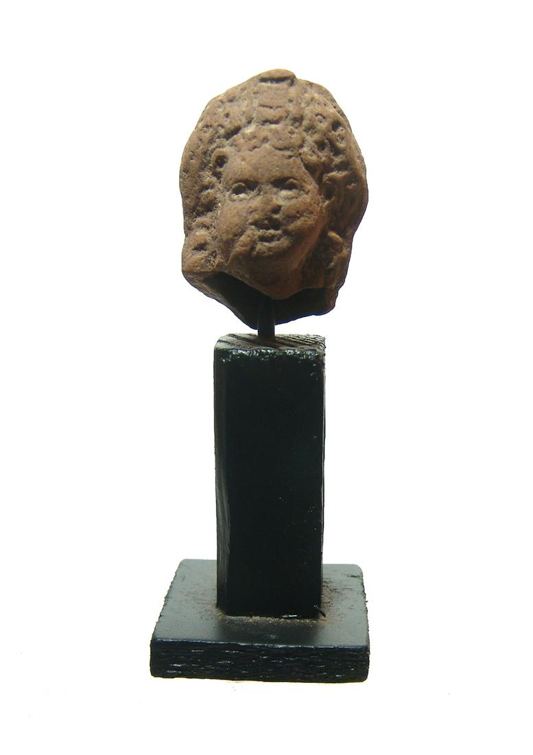 An Egyptian terracotta head of Harpokrates, Ptolemaic: An Egyptian terracotta head of Harpokrates, Ptolemaic, 2nd - 1st Century BC, with detailed features and curled hair, his right finger to his lip. H: 1 3/4 in (4.4 cm). Light deposits, on wood base. Ex
