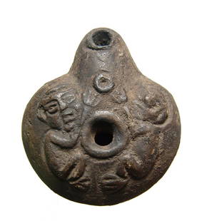 An Egyptian ceramic frog lamp: An Egyptian ceramic frog lamp, c. 2nd - 4th Century AD, of lentoid shape, the body depicting two child-like figures to either side of the fill-hole, the bottom impressed with stylized A. 3 1/8 x 2