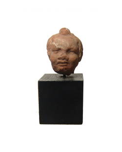 A Greek terracotta head of Eros: A Greek terracotta head of Eros, c. 3rd - 1st Century BC, with rounded features and close-cropped hair. H: 1 1/8 in (2.8 cm). Light deposits. Ex Royal Athena Galleries, New York.