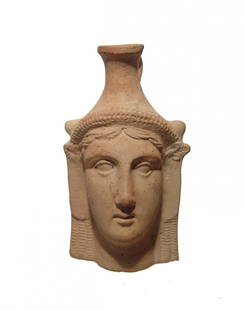 Greek pottery plastic vase depicting a female head: A Greek pottery plastic vase depicting a female head, c. 4th Century BC, with youthful features modeled with plump lips and wide eyes, the hair dressed in long ringlets, surmounted by a wreath with