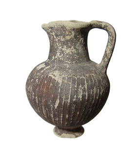A nice Cypriot ribbed oinochoe: A nice Cypriot ribbed oinochoe, c. 4th - 2nd Century BC, with small pedestal foot, trefoil pouring spout and loop handle. The surfaces retain much of the original black slip. H: 7 in (17.7 cm). Light