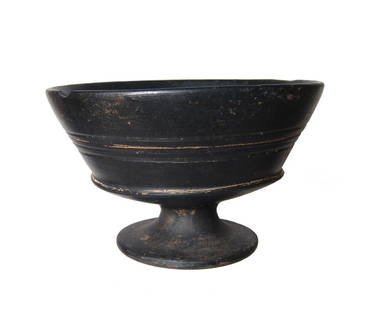An Etruscan bucchero footed chalice: An Etruscan bucchero footed chalice, c. 600 - 525 BC, with short pedestal foot with wide base, the bowl with steep walls with three parallel grooves running around the midsection above ridged