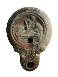 A Roman ceramic discus lamp with erotic scene: A Roman ceramic discus lamp with erotic scene, late 1st Century AD, featuring a woman reclining on a bed with her lover; circular groove border around. The nozzle with shoulder-volutes and a rounded