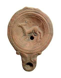 A Roman ceramic discus lamp depicting a hound: A Roman ceramic discus lamp depicting a hound, late 1st - early 2nd Century AD, the discus bordered by ridges and grooves, the nozzle rounded with volutes and with flattened base. L: 3 7/8 in (9.8