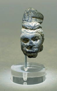 A fine Gandharan stone head: A fine Gandharan stone head, Indus Valley, c. 3rd - 4th Century AD, carved from the blue-gray schist characteristic of the region. It depicts a man with an intricately detailed coif held with a