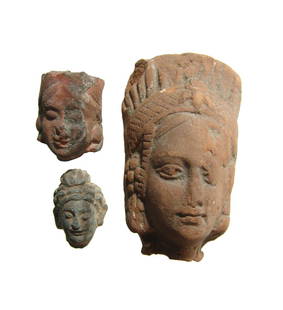 A trio of three nice Indian heads: A trio of three nice Indian heads, c. 3rd - 4th Century AD, two in terracotta, the larger female head with elaborate headdress and jewelry, and one a Gandharan schist head of Buddha. Height from 1 1/8