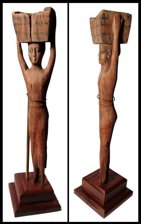 Egypt. Tall wooden servant statue of a woman: A tall wooden servant statue of a woman, wearing a long tunic with sash, holding a square basket on the top of her head. Traces of black pigment remain on eyes and basket. Some loss to feet and a few