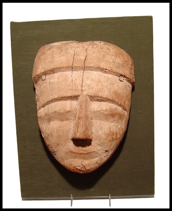 Egyptian large wooden "mummy" mask: A wooden "mummy" mask, Late Period, c.664 - 343 BC. A wooden facial portion of a sarcophagus, devoid of paint or gesso. Features with a solemn expression and mounted to a custom backing. H: 9 ¾" (24.