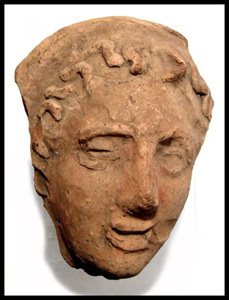 Etruscan terracotta face of a youth: A terracotta Etruscan face of a youth, c.3rd - 2nd Century BC, with handsome features and traces of red-orange paint. His eyes are open and lips lighted parted, hair curled to frame his face. L: 6 3/8