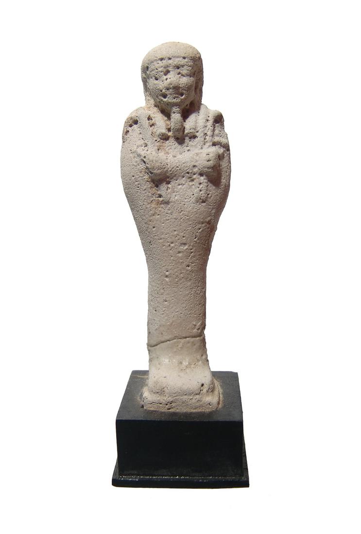 An Egyptian unglazed faience ushabti: An Egyptian unglazed faience ushabti, Late Period, c. 664 - 30 BC, mummiform, wearing tripartite wig and false beard, arms folded across chest, hands holding a pick and hoe, bag over left shoulder, ve