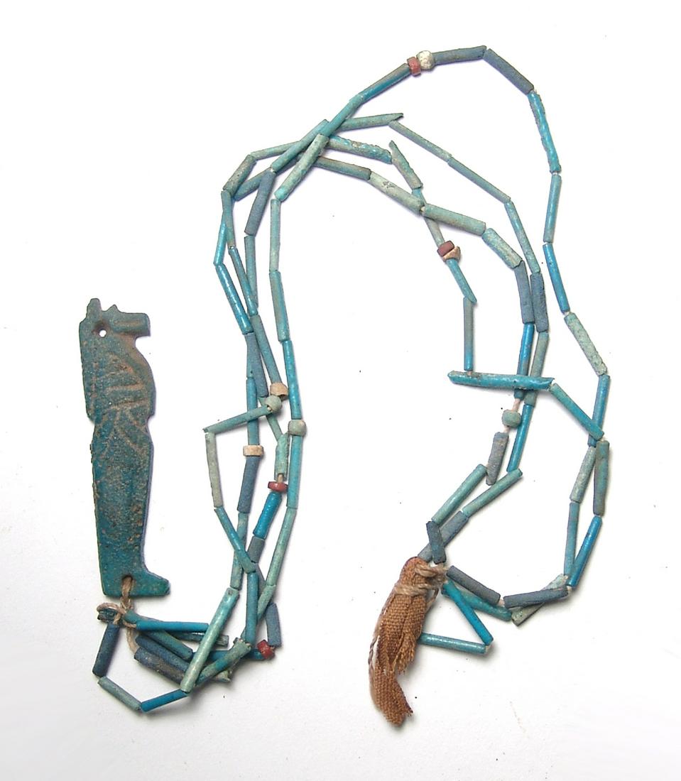 An Egyptian beaded necklace with amulet: An Egyptian beaded necklace with amulet, Late Period - Ptolemaic, c. 664 - 30 BC, including a tuft of Egyptian linen. The tubular beads are of a nice blue fiance and the amulet represents on of the fo