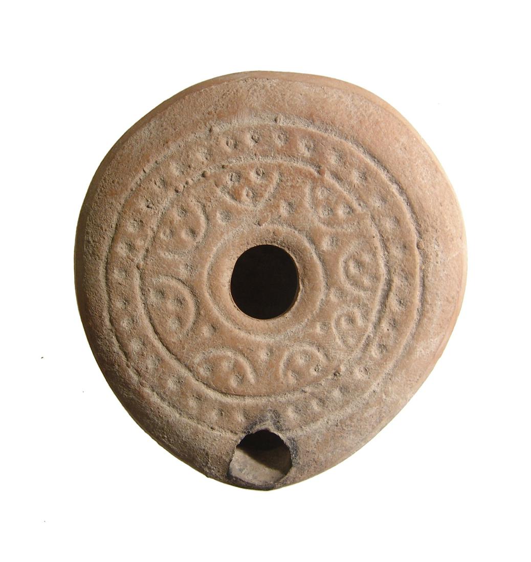 An attractive Byzantine ceramic lamp: An attractive Byzantine ceramic lamp, c. 6th - 7th Century AD, circular in shape and flat, and with bands of impressed decoration around the fill-hole and around the base 3 3/8 x 3 5/8 in (8.5 x 9.2 c