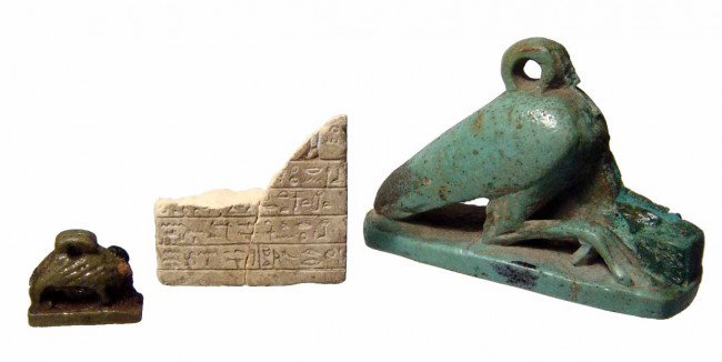 Fragment of a limestone stele and 2 amulets: A fragment of a miniature limestone stele and 2 amulets, Late Period, c. 664-30 BC. The stele is the bottom portion with two complete lines of incised hieroglyphic text and three partial lines. Repair