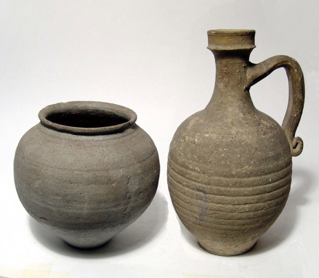 Pair of Roman terracotta vessels: A pair of Roman terracotta vessels. The first a Roman plain buff pitcher, Egypt, c. 1st Century AD, the ovoid body nicely grooved and the handle with a curled end. Intact with some deposits. H: 8 1/4"