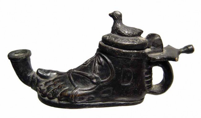 Antique oil lamp in the form of a sandaled foot: An antique oil lamp in the form of a sandaled foot. A nice type imitating a Roman bronze lamp, the toe resting upon the spout, single handle at back, the lid decorated with a seated bird. L: 5 1/2" (1