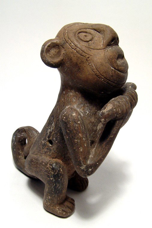Large Tairona monkey ocarina, Colombia: A large Tairona monkey ocarina, Colombia, c. AD 1000-1500. He is depicted seated with tail curled at his back, head looking skyward and holding a stick in his hands. His face is incised with lines aro
