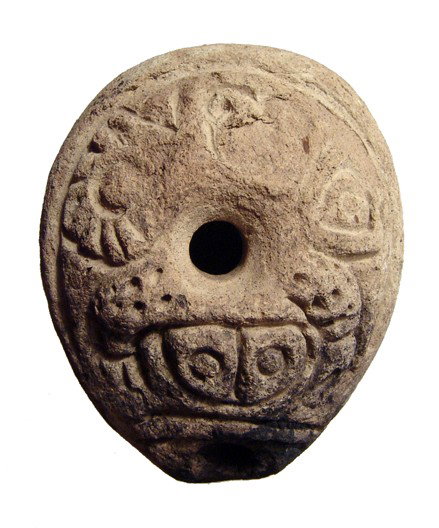 Late Roman Egyptian frog lamp, c.5th Century: A late Roman Egyptian frog lamp, c. 5th Century AD, mold made, ovoid in shape, with rounded carination. Steep inward-sloping rim at the center of stylized frog pattern, nozzle incorporated into the bo