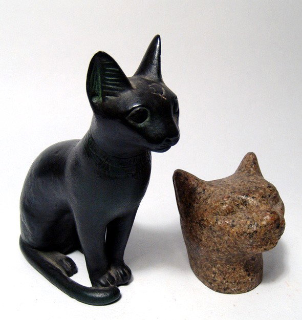 Grand Tour. Egyptian Bastet figures from Egypt: A pair of Egyptian Bastet figures from Egypt, both antique tourist pieces. One is a bronze-looking seated cat and the other is a hydro-stone head. Largest measures 6" (15.2 cm).