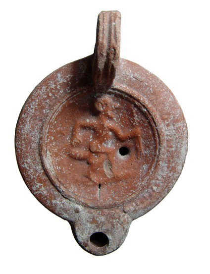 Roman Egypt. Oil lamp with a grotesque: A Roman terracotta discus lamp with a grotesque, Egypt, 2nd - 3rd Century AD. The red-ware lamp with sharp carination and rounded spout, the discus set off from the flat shoulders by a double ridge, t
