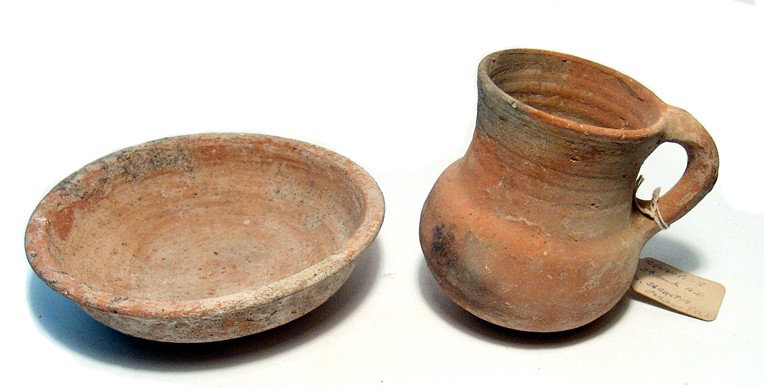 Roman bowl and Byzantine jug: A Roman bowl and Byzantine jug. The Roman terracotta bowl is wheel thrown with simple disk foot and flattened rim. Minor age crack and earthen encrustation, Dia: 5 7/8" (14.9 cm). The Byzantine jug, 5