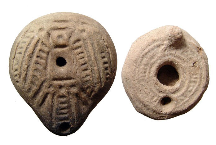 2 oil lamps: Egyptian and Holy Land: A pair of terracotta lamps. The first is a 'frog' lamp from Roman Egypt, c. 3rd - 4th Century AD, with stylized palm motif, maker's mark between concentric circles on base, L: 3 1/2" (8.9 cm); The sec