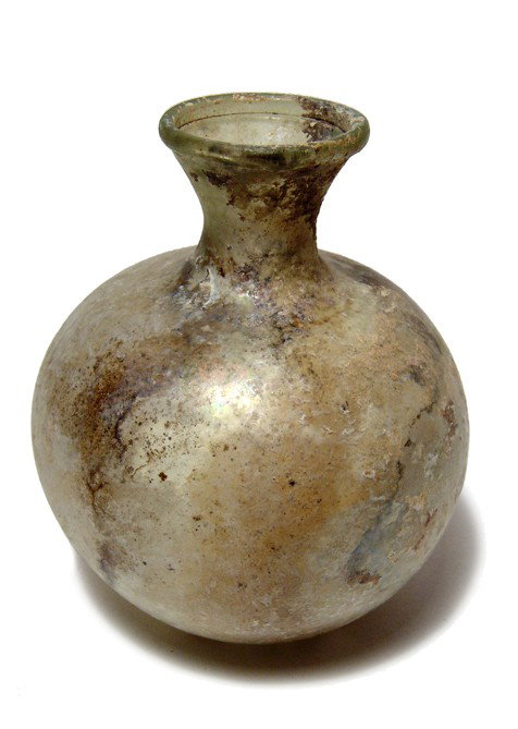 Pale green Roman glass bottle: A pale green Roman glass bottle, 2nd - 3rd Century AD, the body nearly round with indented base, the neck constricted with flared mouth. Intact with light iridescence and earthen deposits. H: 4 1/2" (