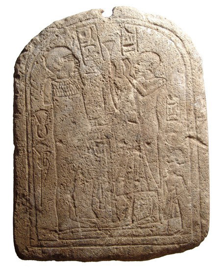 Limestone stele with priest before the god Min: A limestone stele with a priest before the god Min, Late Period, c. 664 - 343 BC, who holds a staff, his penis engorged. Several column of text and a small figure behind the male figure who hands are