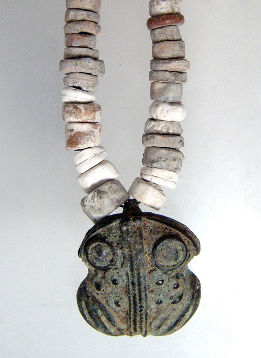 Tairona shell necklace with a frog tumbaga: A Tairona shell necklace with a tumbaga in the form of a frog, Colombia, ca. AD 1000 - 1500. Nicely cast with attractive patination. L: 1 1/2" (3.8 cm). The shell necklace is composed of circular bead