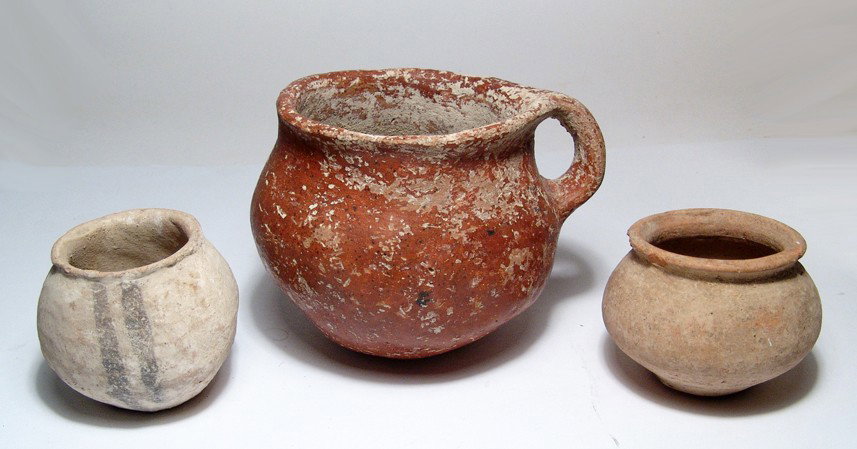 Lot of three early pottery vessels: A lot of three early pottery vessels. The first is an Early Bronze Age I burnished red-ware cup, c. 3100 - 2900 BC, with single handle. Hand formed with shiny surfaces and earthen deposits, H: 3 3/4" 