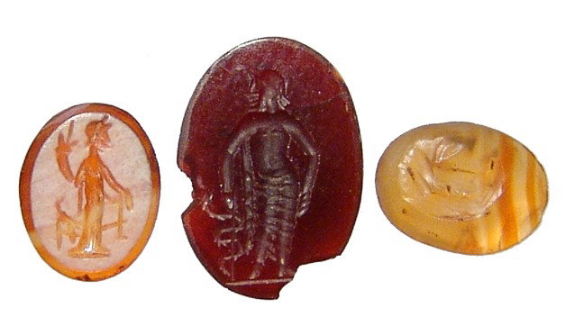 Lot of 3 Roman carnelian intaglios: A lot of 3 Roman carnelian intaglios, c. 1st - 3rd Century AD. Lot includes a dark colored example depicting the god of medicine Asklepios resting on his serpent-staff, 12 x 9mm; A bi-color stone depi