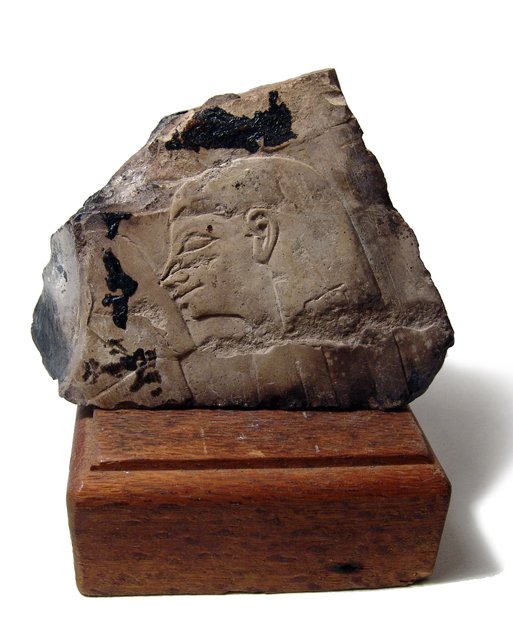 Egyptian limestone relief, New Kingdom Egypt: An attractive Egyptian limestone relief, New Kingdom, c. 1570 - 1075 BC, feature a female head in profile, uncertain objects before her. Some dark concretions and deposits. 4 3/4" x 3 3/4" (12.1 x 9.5