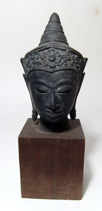 Bronze head of Buddha, Thailand: A bronze head of Buddha, Thailand, c. 18th - 19th Century, wearing a headdress with floral border and flanged at each side, his ushnisha with three tiers, his ear lobes elongated with bands near the e