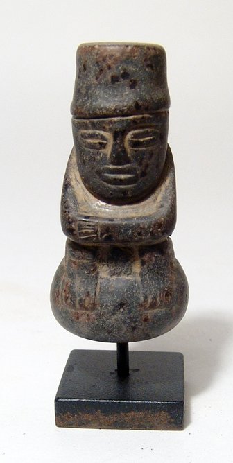 Stone pestle, seated man, Colombia, Muisca: A small stone pestle in form of seated man, Colombia, Muisca, c. AD 1000 - 1550. with stylized features, arms folded across his chest and resting on his bent knees. H: 2 1/4" (5.4 cm). Mounted on a cu