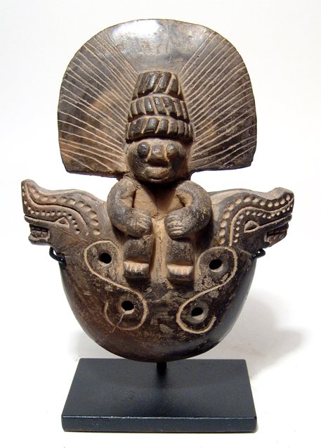 Tairona ocarina, deity on a jaguar throne: A large Tairona black-ware ocarina depicting a deity on a jaguar throne, Colombia, AD 1000 - 1500. The figure wears a large headdress with three tiered cap and large feathered fringes, his features ar