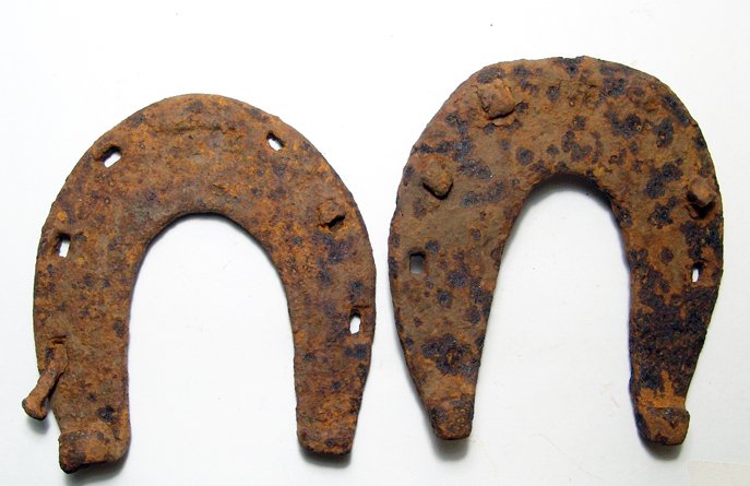 Pair of Medieval wrought iron horseshoes: A pair of Medieval wrought iron horseshoes,13th to early 16th Century, both U-shaped with plain inner edge and wide heels with bent ends, one with narrower ends than the other. Three rectangular nail 